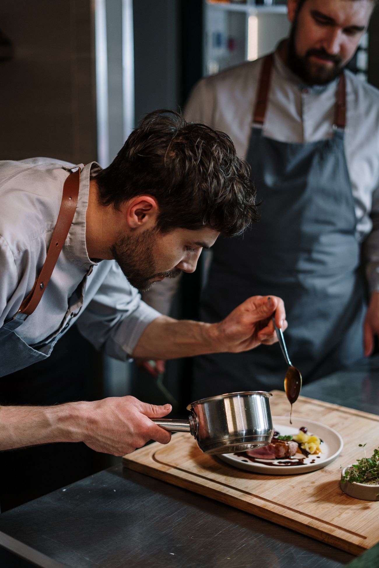 A grill cook finishing a dish with a spoonful of sauce