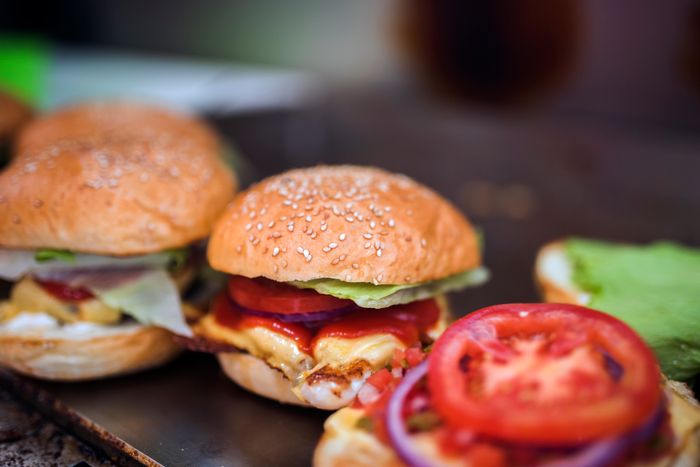 Two burgers and a tomato on a board